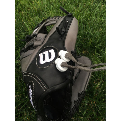 A black and gray Wilson baseball glove with two white All Star GloveLock (4 Pack): GL-4PACK attached by gray strings, resting on green grass to keep the glove secure.