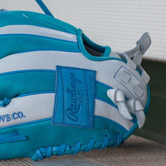 A close-up of a blue and white Rawlings baseball glove resting on a wooden surface. The glove features prominent stitching and branding on a blue patch.