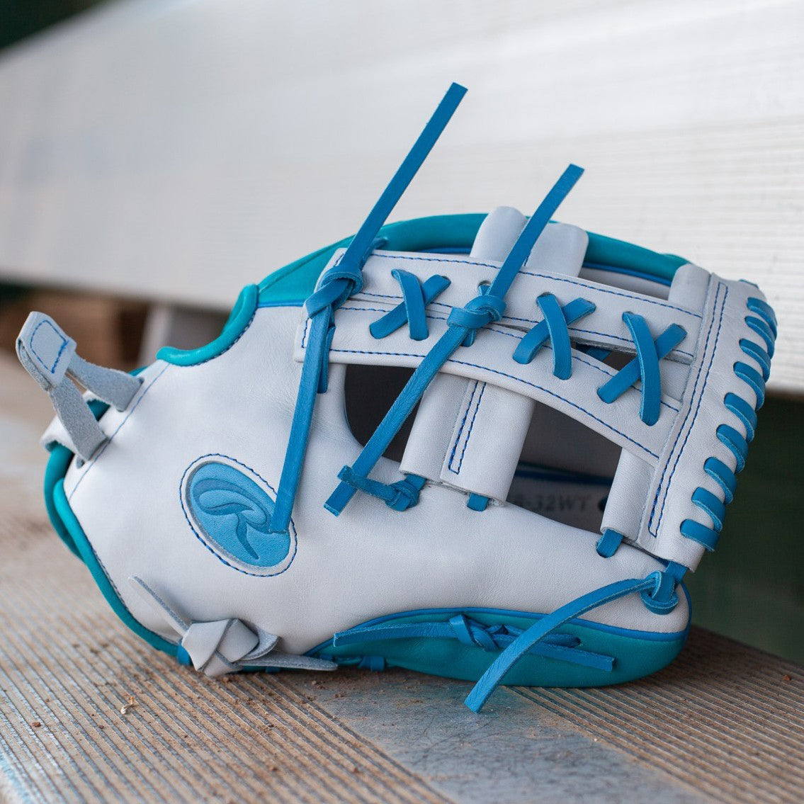 A white baseball glove with blue laces and trim rests on wooden benches, close to a wall.
