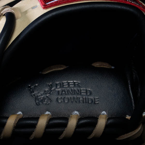Close-up of a baseball glove’s interior, showing the embossed text “DEER TANNED COWHIDE” along with a small deer graphic, surrounded by beige and black leather details.