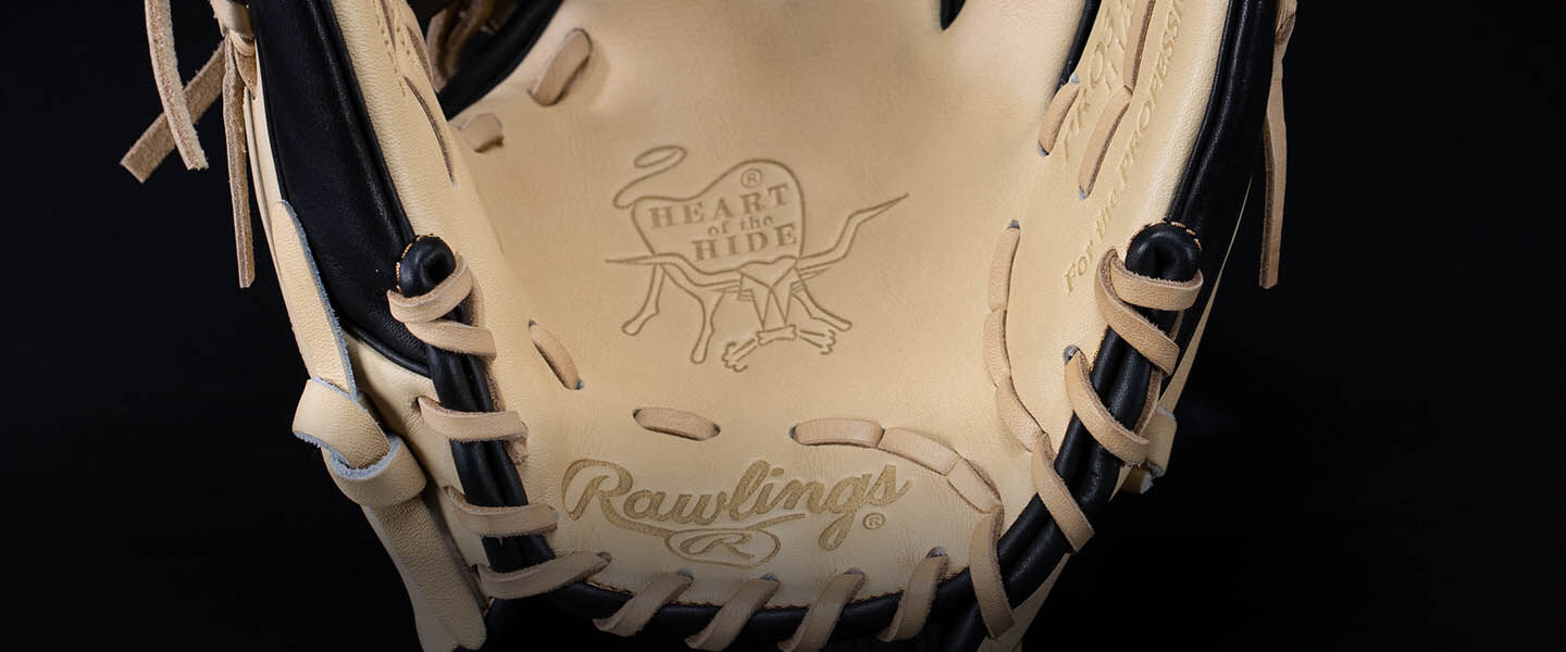 Close-up of the inside palm of a Rawlings baseball glove, showing tan leather with the “Heart of the Hide” logo and Rawlings branding embossed on the surface. Black and tan laces are visible around the edges.