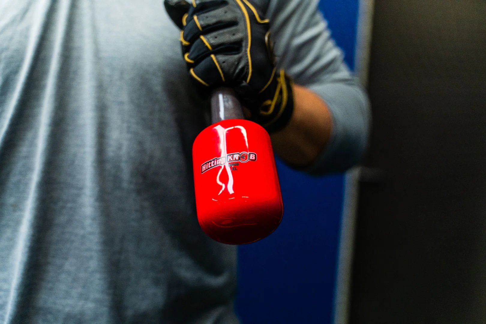 A person wearing a grey shirt and black gloves holds a red, cylindrical object labeled KNOB with a metallic handle, against a blurred blue and black background.
