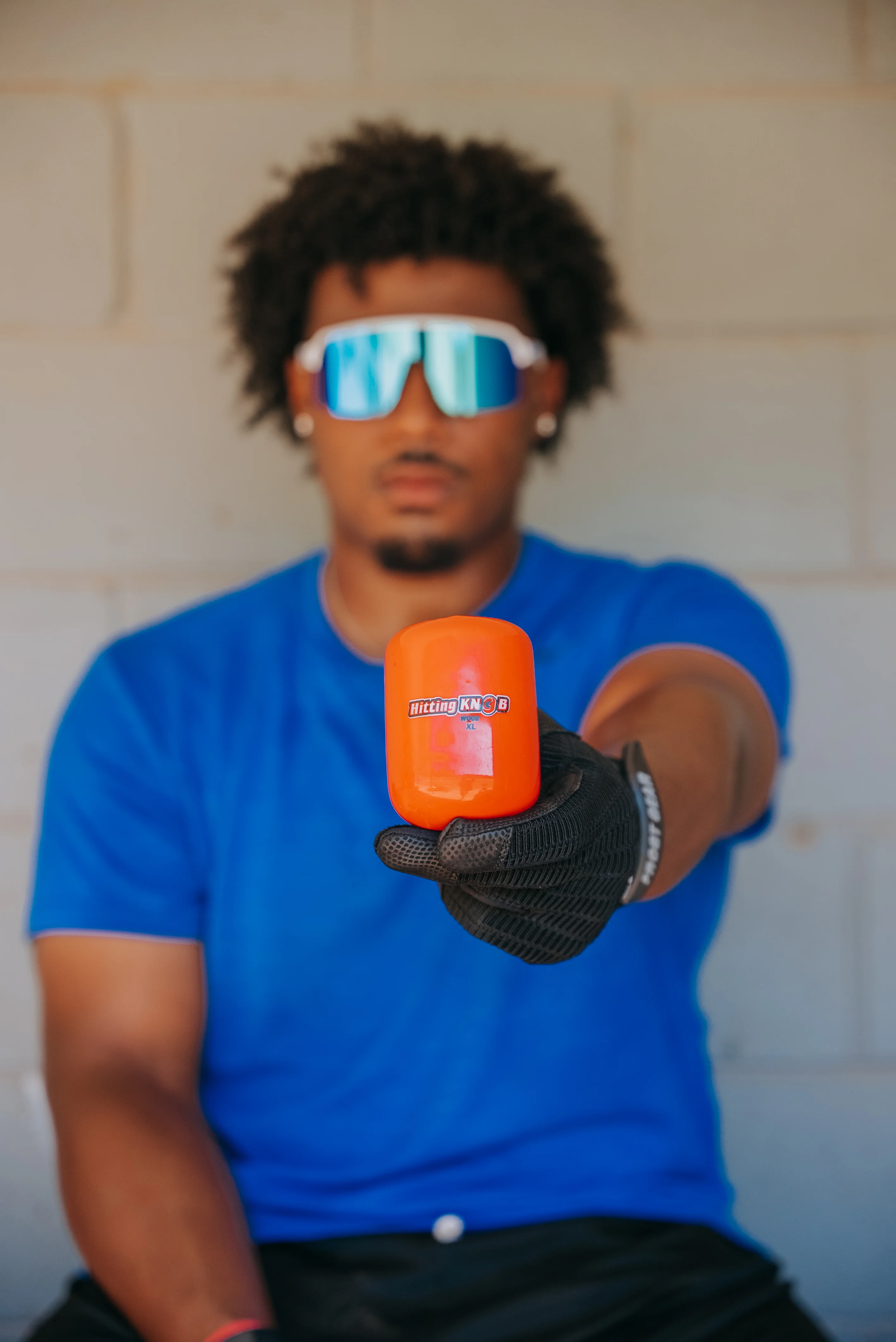 A person wearing a blue shirt, reflective sunglasses, and a black glove holds an orange sliding aid labeled Sliding Pro toward the camera, with a neutral background.