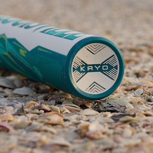 Close-up of the teal and white Louisville Slugger 2026 Kryo (-8) Fastpitch Softball Bat (WBL4137010) with GO-EX1 Barrel System, lying on sand and seashells.