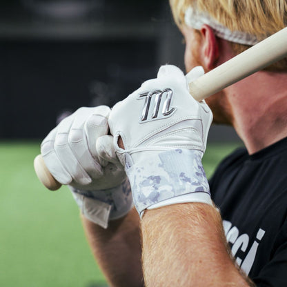 A youth with light hair in a black shirt grips a bat, preparing to swing indoors, while wearing Marucci REMX Youth Batting Gloves (MBRMXY) featuring the silver Marucci logo.