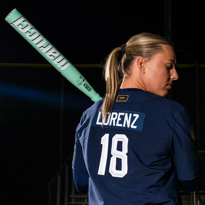 A softball player in a navy jersey with LORENZ and number 18 on the back holds a 2025 Marucci ASURA (-9) Fastpitch Softball Bat: MFPAS9 (DEMO), highlighting its Gap Sync barrel tech against a dark background.