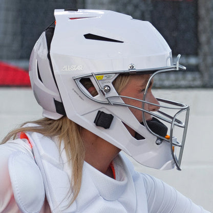 A person wearing an All Star PHX Paige Halstead MVP Pro Lite Hockey Style Catcher’s Helmet (MVP-5-PHX-LT) in white, along with a matching chest protector, is seen in profile view—evoking the signature style of fastpitch gear inspired by Paige Halstead and ideal for softball or baseball.