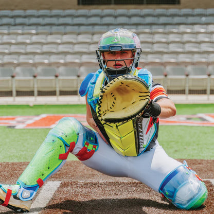 Wearing the All Star MVP Pro Catcher's Kit (CKCC-5), a catcher crouches behind home plate with mitt ready, colorful gear on display and empty stadium seats in the background.