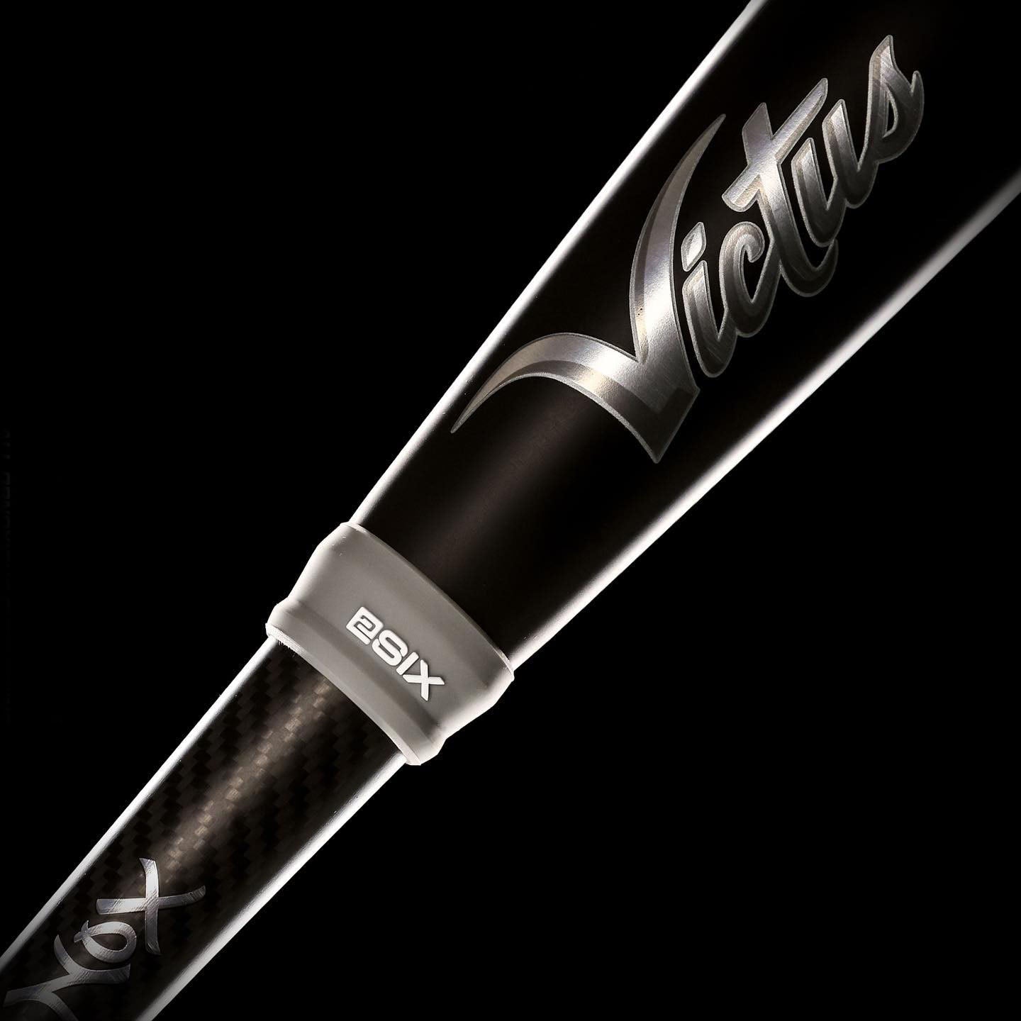 Close-up of a black Victus baseball bat with a carbon fiber texture and “Victus” written in silver script. The bat features a white ring labeled 29X near the handle against a black background.