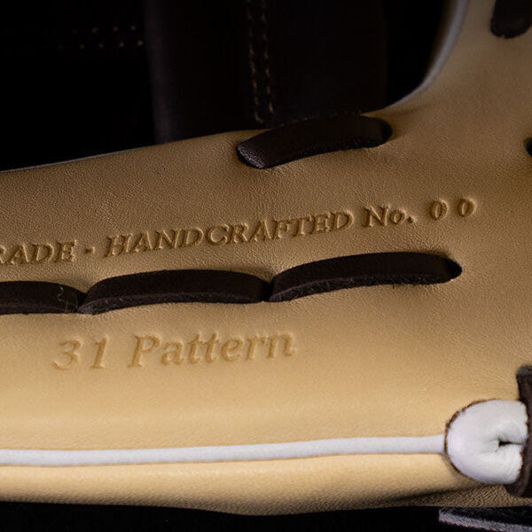 Close-up of tan and brown leather baseball glove, showing embossed text that reads “HANDCRAFTED No. 00” and “31 Pattern” along the inside of the glove.