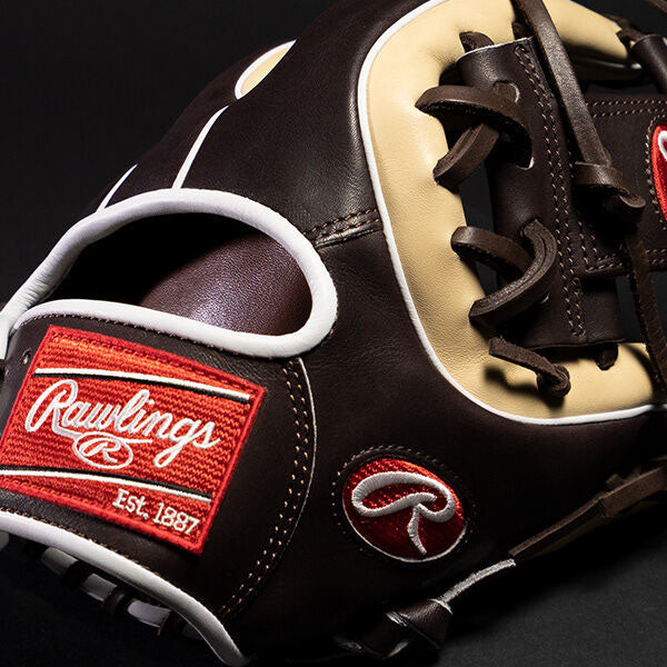 Close-up of a brown and beige Rawlings baseball glove featuring red and white Rawlings logo patches and detailed stitching against a black background.