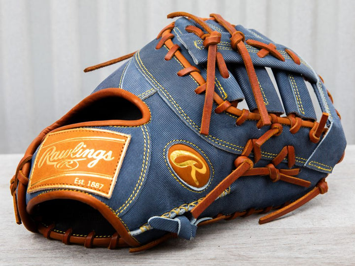 A blue Rawlings baseball glove with brown leather lacing and trim, featuring a gold Rawlings logo patch and label, resting on a light wooden surface.