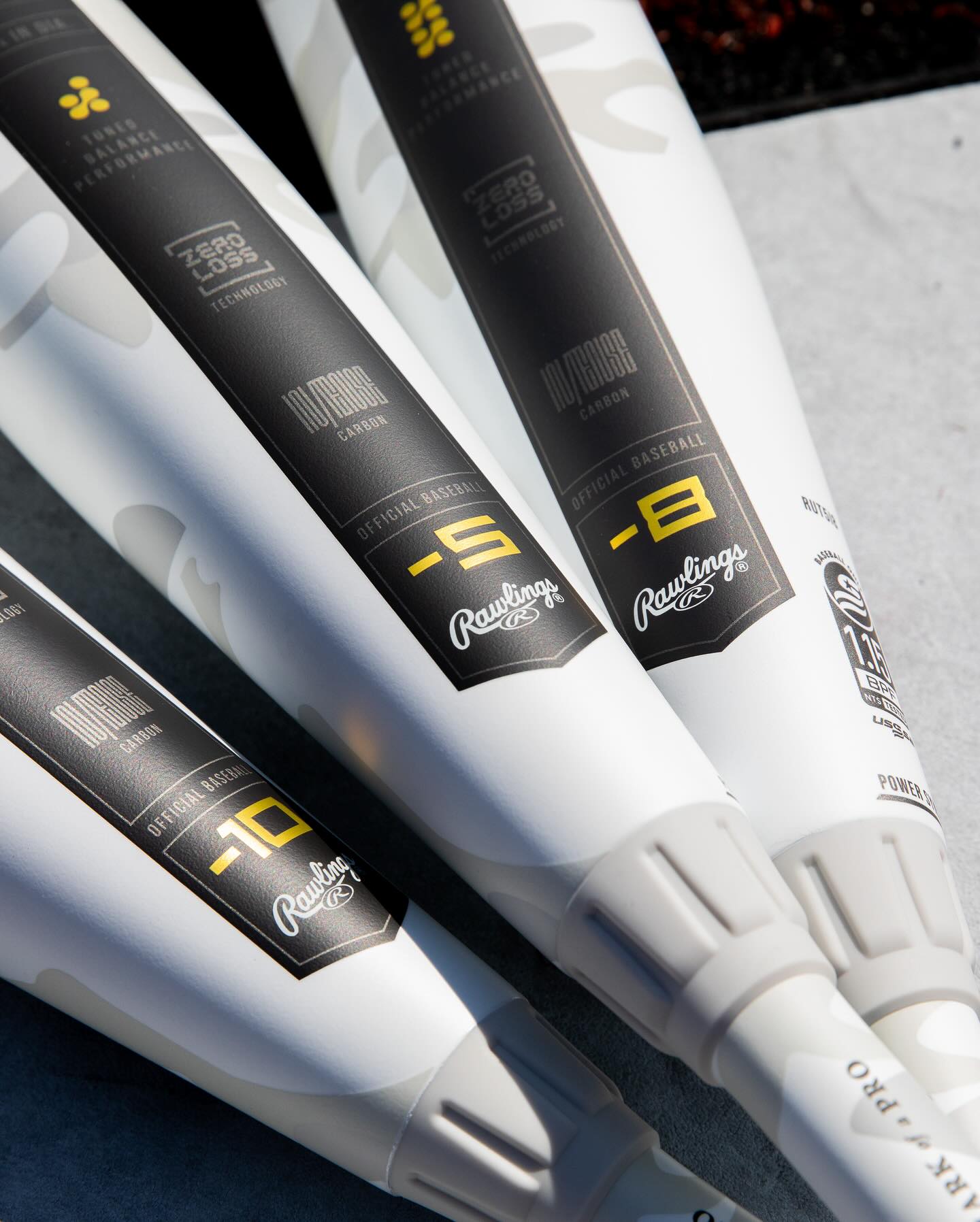 Close-up of four white Rawlings bats, featuring the 2025 Rawlings Icon (-5) 2 3/4" USSSA Baseball Bat (RUT5I5), side by side with dark gray labels and yellow and white text showing model details and drop weights like -10, -8, and -5.