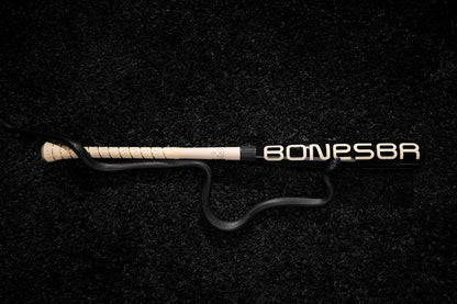 A black snake is coiled around a Warstic 2025 Bonesaber Hybrid Black Cobra (-3) BBCOR Baseball Bat, resting on a textured black surface.