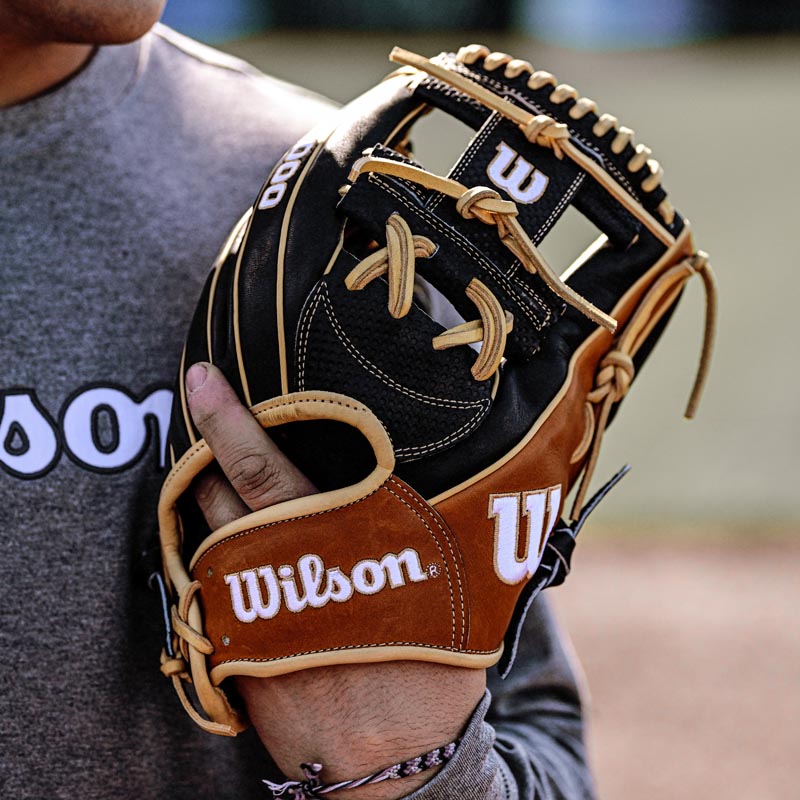 A person wearing a gray Wilson shirt holds a Wilson baseball glove with tan and black leather lacing, featuring the brand’s logo prominently displayed.