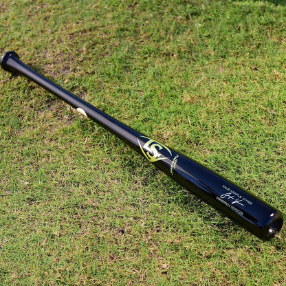 A Louisville Slugger MLB Prime Signature Series CY22 Christian Yelich Game Model Wood Baseball Bat (WBL2435010), featuring black wood with gold and white accents, rests on green grass.