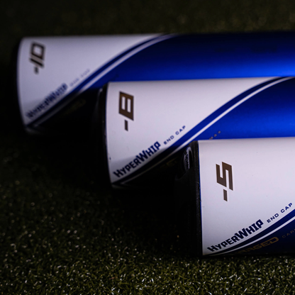 Close-up of three AXE Avenge Pro USSSA Baseball Bat handles, including the 2023 AXE Avenge Pro (-5) L199K (USED), with white HyperWhip End Caps and 3-piece composite design on a textured green surface.