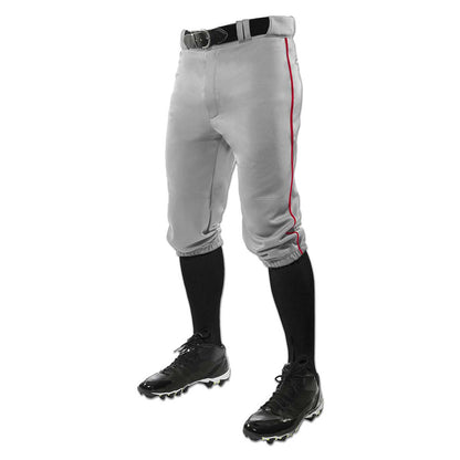 A person wears Champro Sports Adult Triple Crown Knicker Baseball Pants with red piping (BP101A), made of gray pro-weight fabric, paired with a black belt, knee-high black socks, and black cleats; only the lower body is shown.