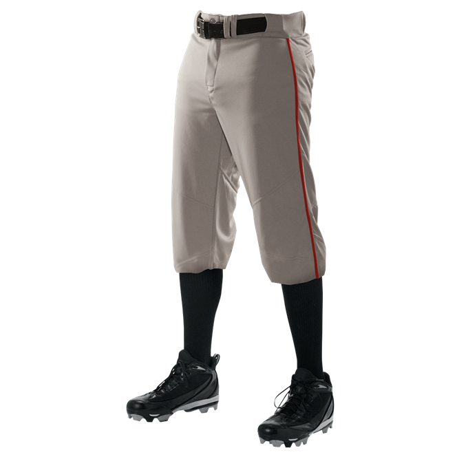 A person wears Alleson Adult Crush Knicker Baseball Pants with Piping (655PKB) in gray by Alleson, featuring a red side stripe, styled with black knee-high socks, cleats, and belt—shown waist down against a white background.