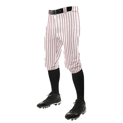 A person wears Champro Sports Triple Crown Pinstripe Knicker Baseball Pants (BPPINKA) in white with red stripes, a black belt, black knee-high socks, and black cleats, standing against a white background; upper body not visible.