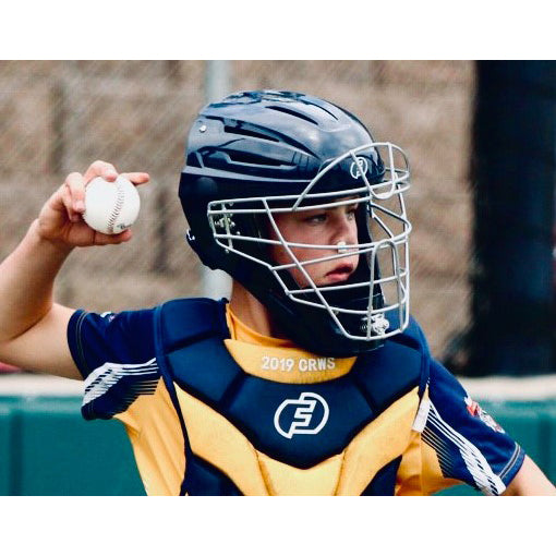 A young catcher wearing the Force3 Hockey Style Defender Catcher's Helmet (BD22) by Force3 and protective gear prepares to throw a baseball, standing out against the blurred backdrop of the fence and field.