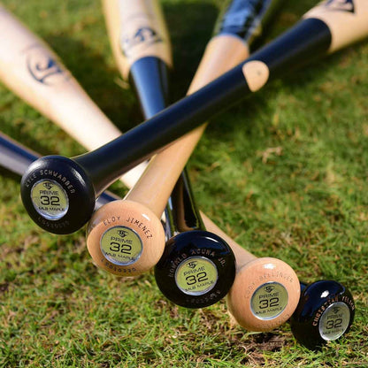 Five Louisville Slugger wooden baseball bats, including the MLB Prime Signature Series CY22 Christian Yelich Game Model (WBL2435010), are arranged fan-like on grass. The black-handled bats have knobs labeled with player names and numbers 32 and PRIME.