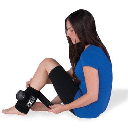 A woman in a blue shirt sits on the floor, securing a Bownet ICE20 Elbow / Small Knee Ice Compression Wrap (ICE-ELBOW-SM KNEE) around her knee. The black wrap features a circular control unit and is set against a plain white background.