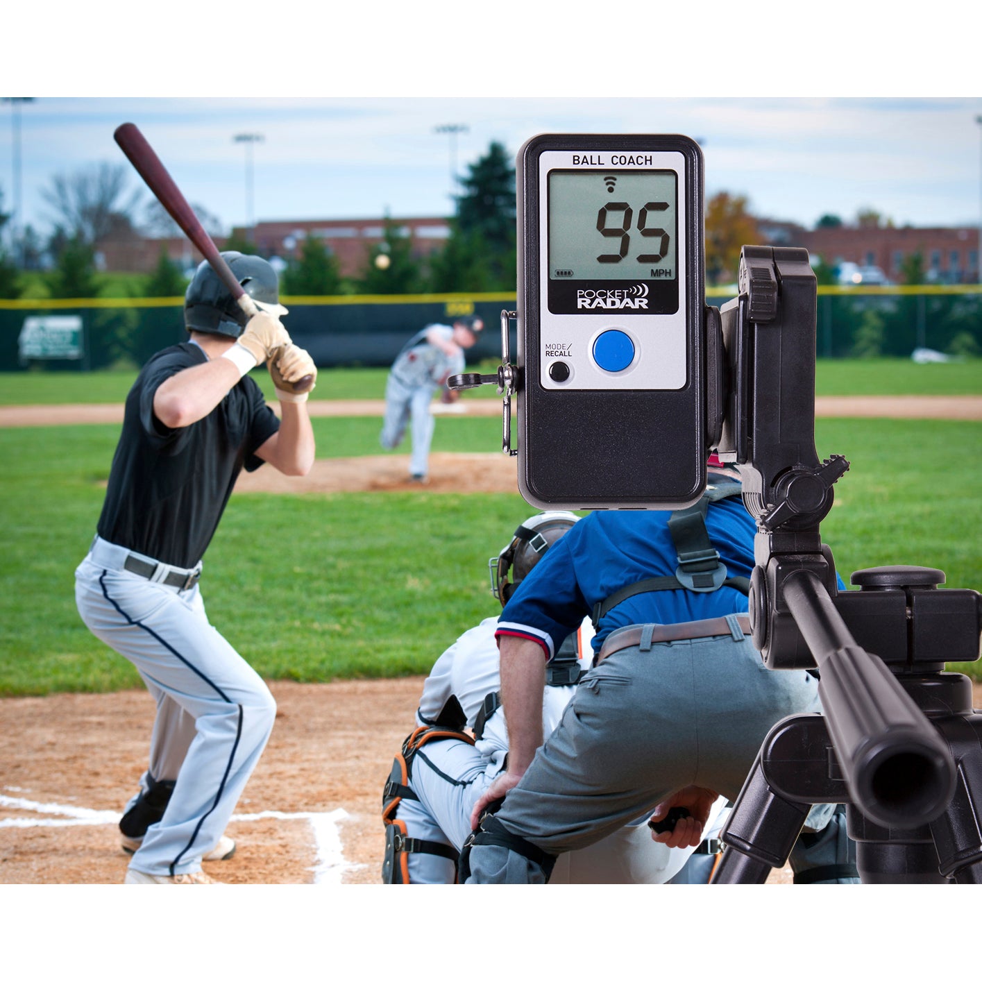 The Pocket Radar Ball Coach Radar (PR1000-BC) by Pocket Radar, mounted on a tripod, shows 95 MPH to measure ball speed as a pitcher throws to a batter, with an umpire and catcher behind home plate during the game.