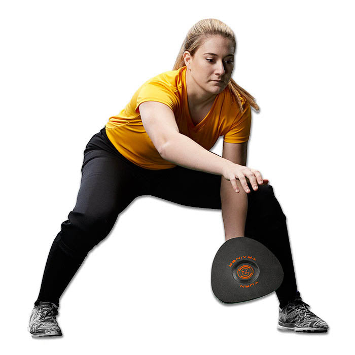 A woman in a yellow shirt and black pants bends her knees and leans forward, holding the Champro Sports Turn-2 Infield Training Glove (CPTT) with one hand, as if practicing ground ball receiving for baseball training.