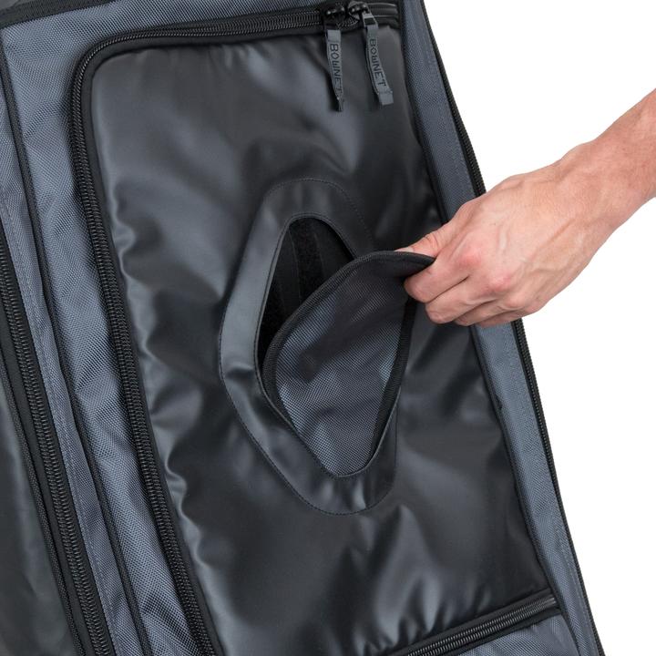 A hand opens a small oval flap on a black and gray Bownet Commander Wheeled Catcher's Bag (BN-COMMANDER BAG), revealing an inner compartment.