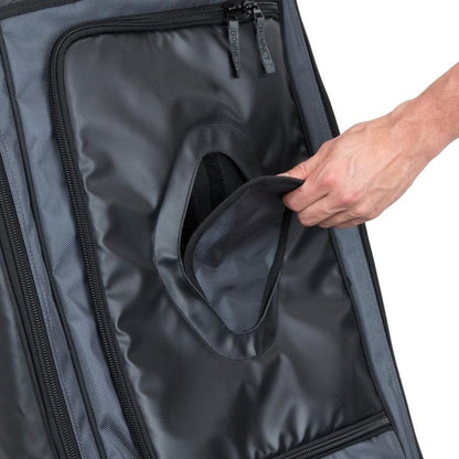 A hand opens a small oval flap on a black and gray Bownet Commander Wheeled Catcher's Bag (BN-COMMANDER BAG), revealing an inner compartment.