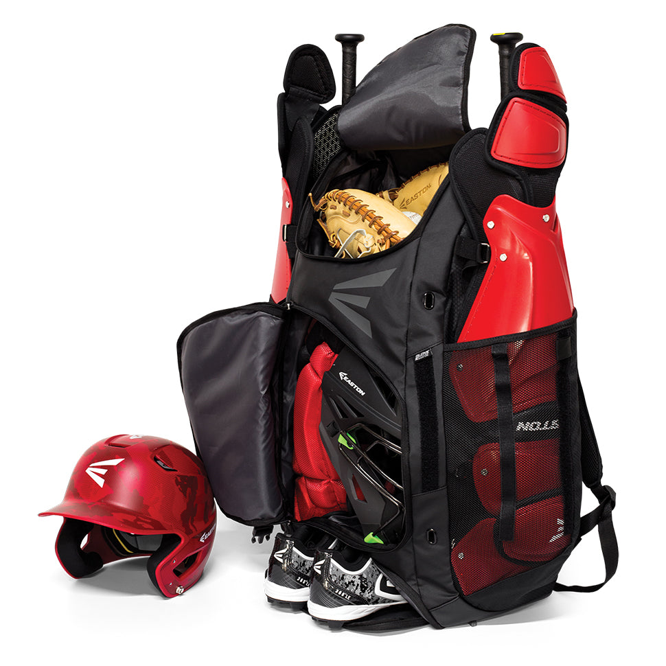 An Easton E610 Catcher's Backpack (E610CBP CATBP) in black and red stands open, displaying a glove, bat, cleats, helmet, and protective gear inside, with a red helmet and black cleats placed beside it.