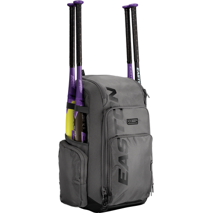 A gray Easton Roadhouse Backpack: EBA004 holds two purple and black baseball bats in side pockets, featuring multiple zippered compartments. The EASTON brand name is printed vertically on the front of this versatile bat bag.