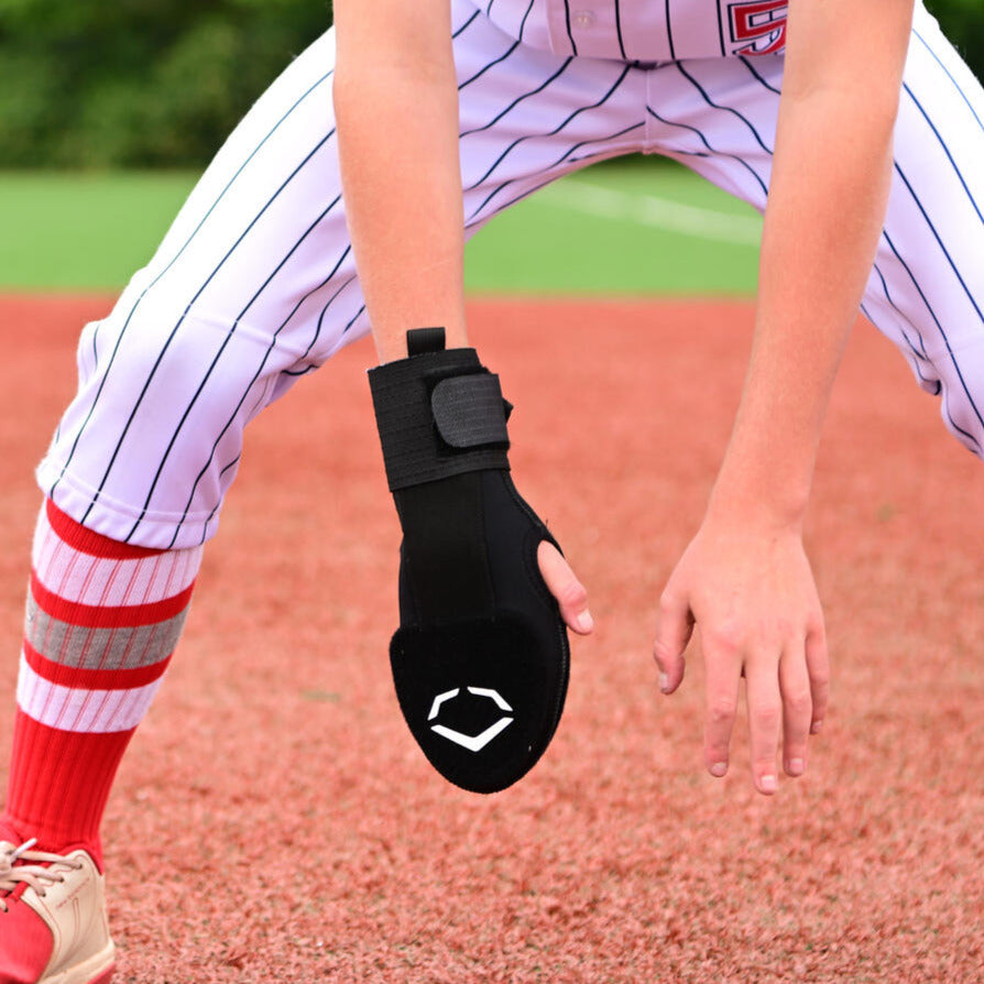 A baseball player in a white pinstriped uniform and red socks crouches on the field, wearing the EvoShield Youth Sliding Mitt: WB573380 by EvoShield for added protection.