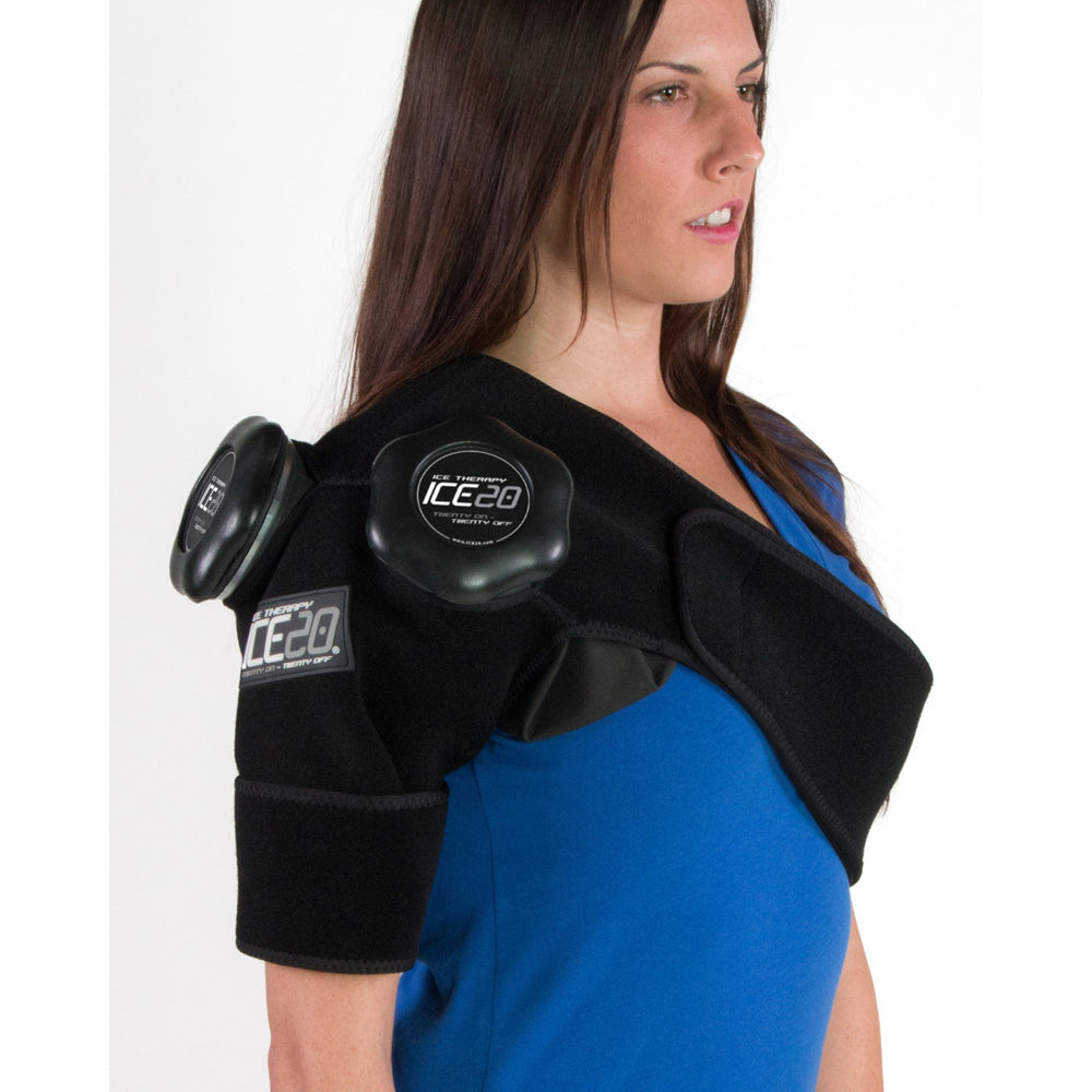 A woman in a blue shirt wears the Bownet ICE20 Double Shoulder Ice Compression Wrap (ICE-Dbl-Shoulder), which features built-in refillable ice packs for targeted therapy on her right shoulder and upper arm, against a plain white background.