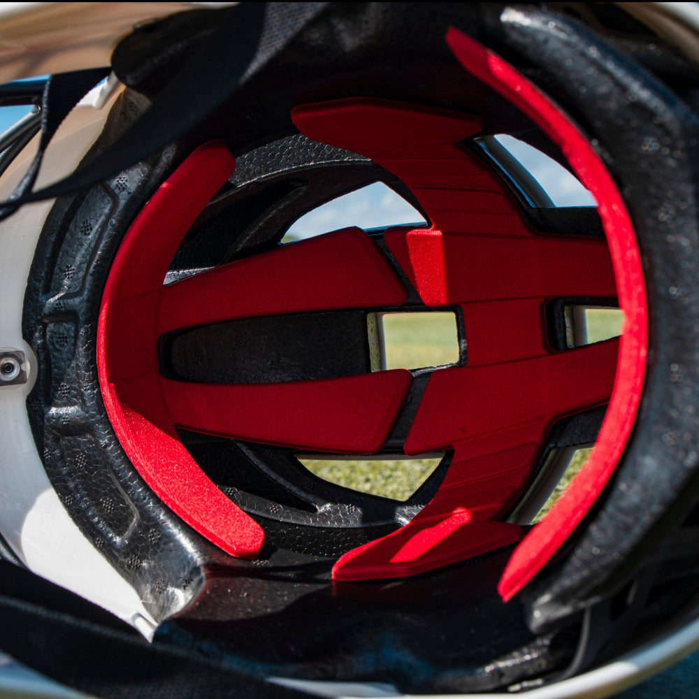 Close-up inside the Easton Hellcat Slowpitch Fielding Helmet (EHCATH) by Easton, highlighting red and black padding in a white shell, with a blurred outdoor background—essential protective gear for slowpitch players.