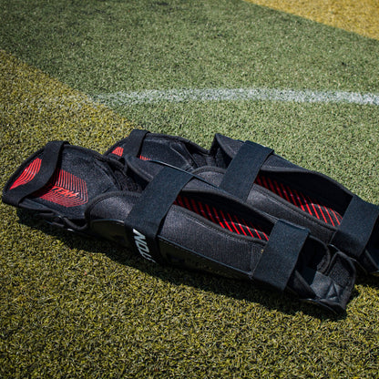 A pair of Easton Hellcat Slowpitch Fielding Leg Guards (EHCATL) in black rests on a green field.