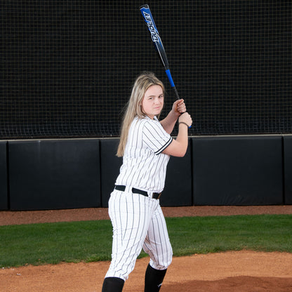 A softball player in a white pinstriped uniform stands in a batting stance, gripping the 2023 Dudley Doom (-10) Fastpitch Softball Bat: DDFP10 by Dudley over her shoulder, focused and ready to hit.