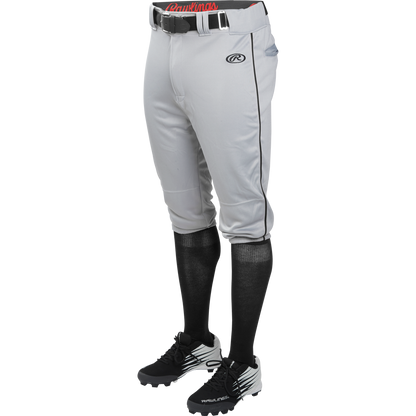 A person wears Rawlings Adult Launch Knicker Baseball Pants with black piping in Blue Grey/Black, featuring the Rawlings logo on the left thigh, paired with a black belt, black knee-high socks, and black cleats with white accents.