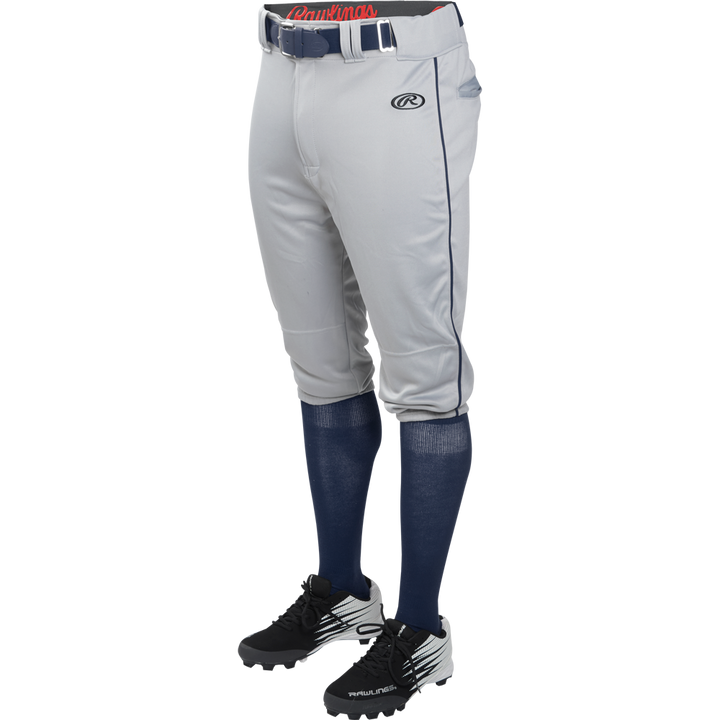 A person wears Rawlings Adult Launch Knicker Baseball Pants with Piping (Blue Grey/Navy), styled with a blue belt, blue knee-high socks, and black and white cleats, shown waist down against a plain background.