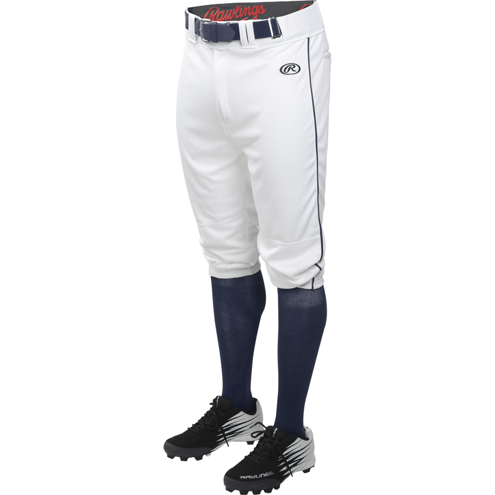A person is shown from the waist down wearing Rawlings Adult Launch Knicker Baseball Pants with Navy piping in white/navy, a black Rawlings belt, navy socks, and black Rawlings cleats against a white background.