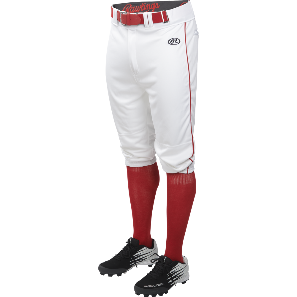 A person in Rawlings Adult Launch Knicker Baseball Pants with white/scarlet piping, a red Rawlings belt, red socks, and black cleats stands against a plain white background.