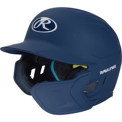 The Rawlings Mach Matte Batting Helmet with EXT Flap (MACHEXT) is a navy blue helmet featuring a protective face guard, black interior padding, and white Rawlings logos on the front and side.