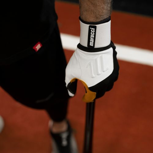 A person wearing Marucci Blacksmith Adult Batting Gloves (MBGBKSMFW) with a durable goatskin palm grips a baseball bat while standing on a red and black surface with a white line nearby.