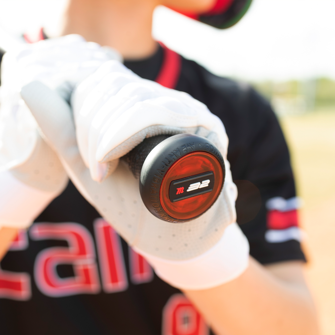 A baseball player in white gloves and a black jersey grips the end of a Marucci 2021 CAT9 (-8) 2 3/4" USSSA Baseball Bat (MSBC98), with "32" on the knob, set against an out-of-focus sunlit field.
