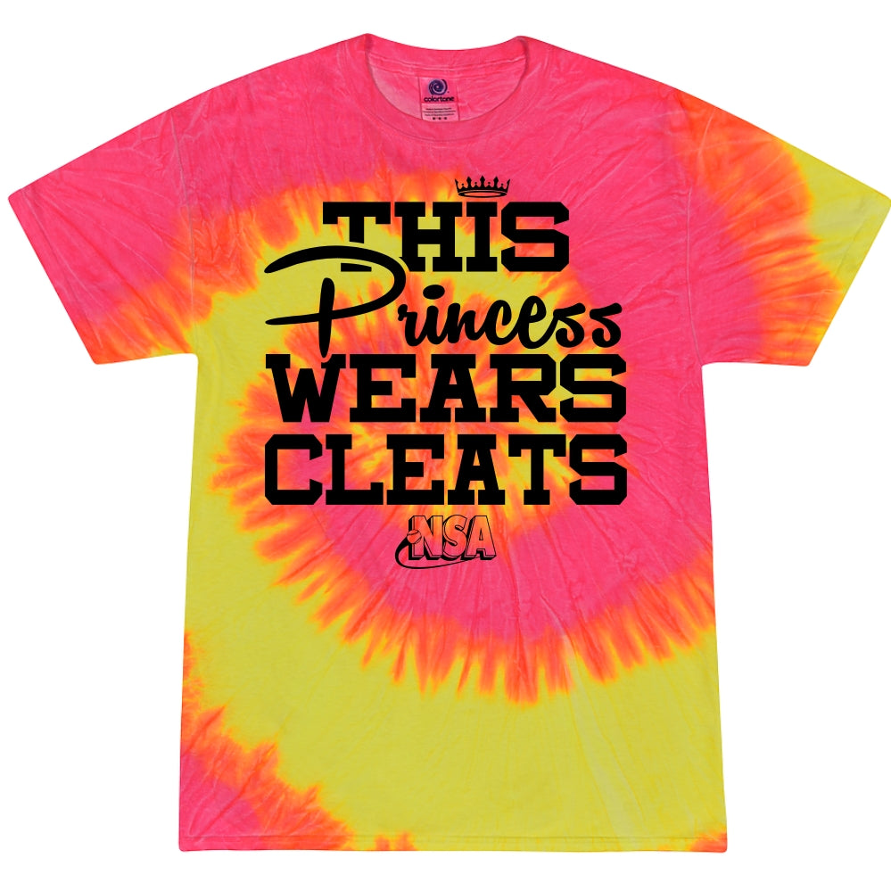 The DSG Apparel NSA This Princess Wears Cleats Short Sleeve Shirt features pink and yellow tie-dye, bold black and yellow text, a small crown, and the NSA logo—perfect for National Softball Association fans.