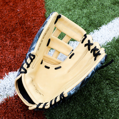 A Rawlings REV1X 12.75" Baseball Glove (REV3039-6) in tan and black rests open on artificial turf, beside a white line separating the green and red field sections.