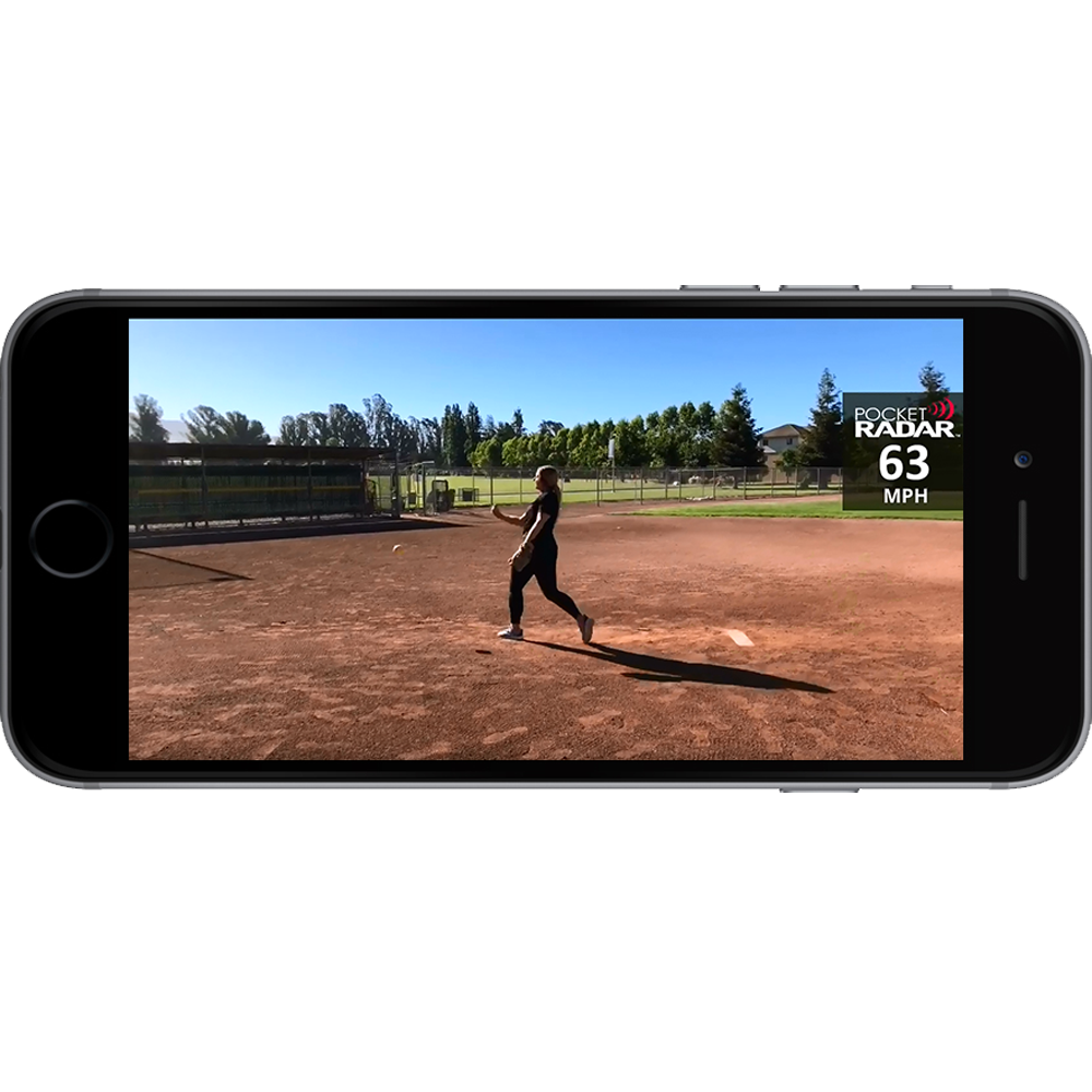 A smartphone shows a softball pitcher mid-throw on a field, with the Pocket Radar Smart Coach Radar: SR1100 by Pocket Radar app displaying a 63 MPH speed. Trees and a fence appear in the background beneath a clear sky.