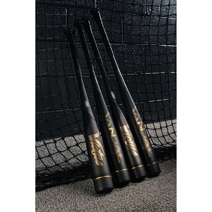 Four black and gold Victus Vandal 2 (-8) USSSA baseball bats stand upright against a netted wall on gray carpet, showcasing their sleek, modern design—ideal for serious players seeking top performance.