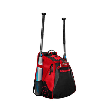 The DeMarini Voodoo Junior Backpack: WTD9106 in red and black stands upright, displaying two bats in its side sleeves, a blue water bottle in a mesh pocket, a visible front zipper, and the DeMarini logo.